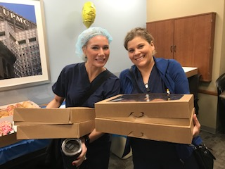 "Two CRNAs holding boxes of donuts"