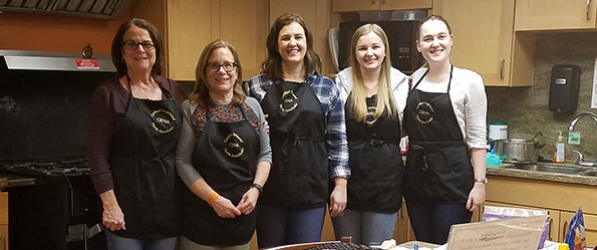 "A group of CRNAs in aprons pose in a kitchen"