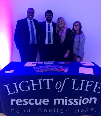 "Two men and two women pose behind a table for Light of Life rescue mission with resources and pamphlets"