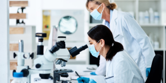 Photo of a young medical researcher working in a lab with their colleague in the background